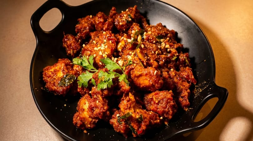 A black plate filled with spicy fried chicken, garnished with cilantro and chopped nuts.