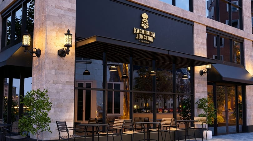 Exterior of Kachiguda Junction restaurant with outdoor seating, large windows, and a black and gold sign.