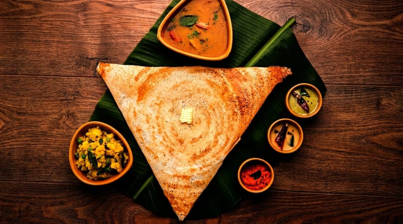 A triangular dosa with butter, served on a banana leaf with sambar, potato curry, and chutneys.