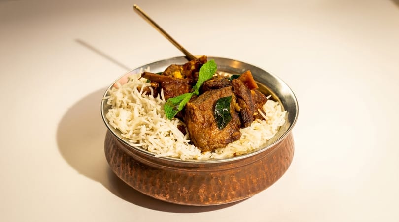 A copper bowl filled with white rice, topped with meat curry and garnished with mint leaves.