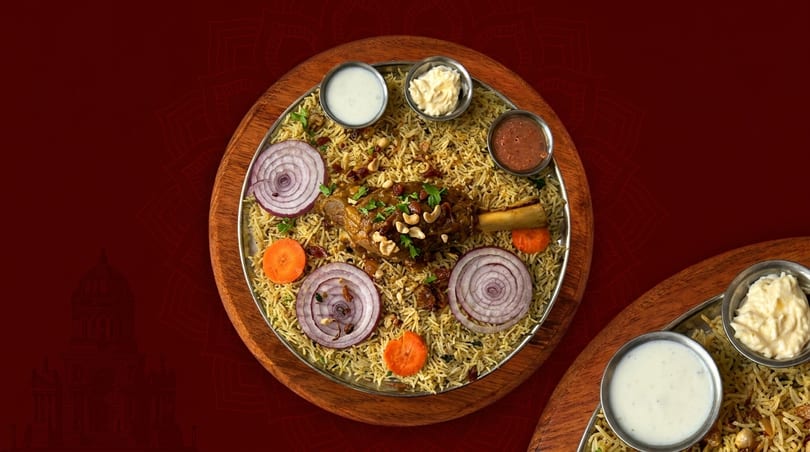Mandi rice with lamb shank, garnished with cashews, raisins, onions, and carrots, served with sauces.