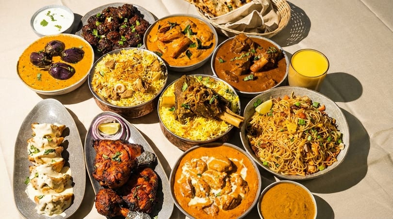 A lavish spread of Indian dishes, including curries, biryani, noodles, and tandoori chicken.